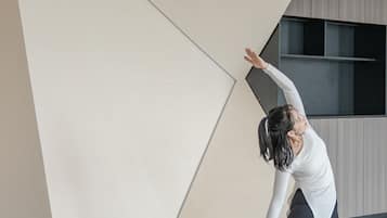 Eine Person führt eine Yoga-Pose auf einer Matte in einem Raum mit modernem Design durch, inklusive schräger Decke und Holzboden.