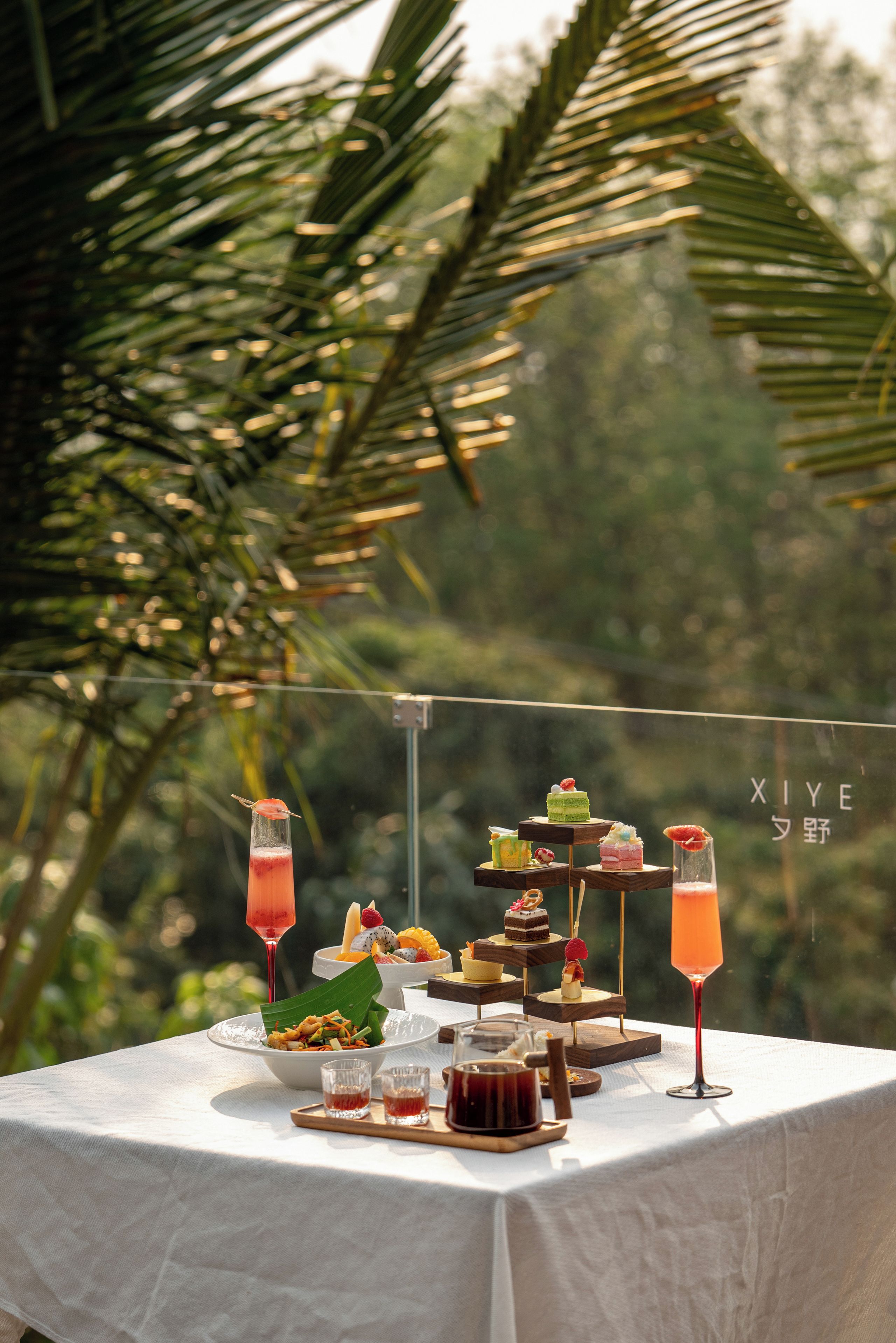 Una mesa con diversos postres y bebidas, con un fondo tropical.