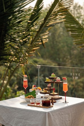 A table set with various desserts and drinks, with a tropical background. - XiyeSeclusionResortHotel (Xishuangbanna Dai)