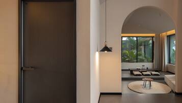 A modern interior with a sliding door, a hanging pendant light, a seating area with cushions, and a view through a large window.