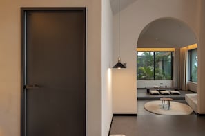 A modern interior with a sliding door, a hanging pendant light, a seating area with cushions, and a view through a large window. - XiyeSeclusionResortHotel (Xishuangbanna Dai)