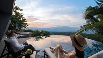 A couple relaxing by a pool with a view of mountains and a cityscape.