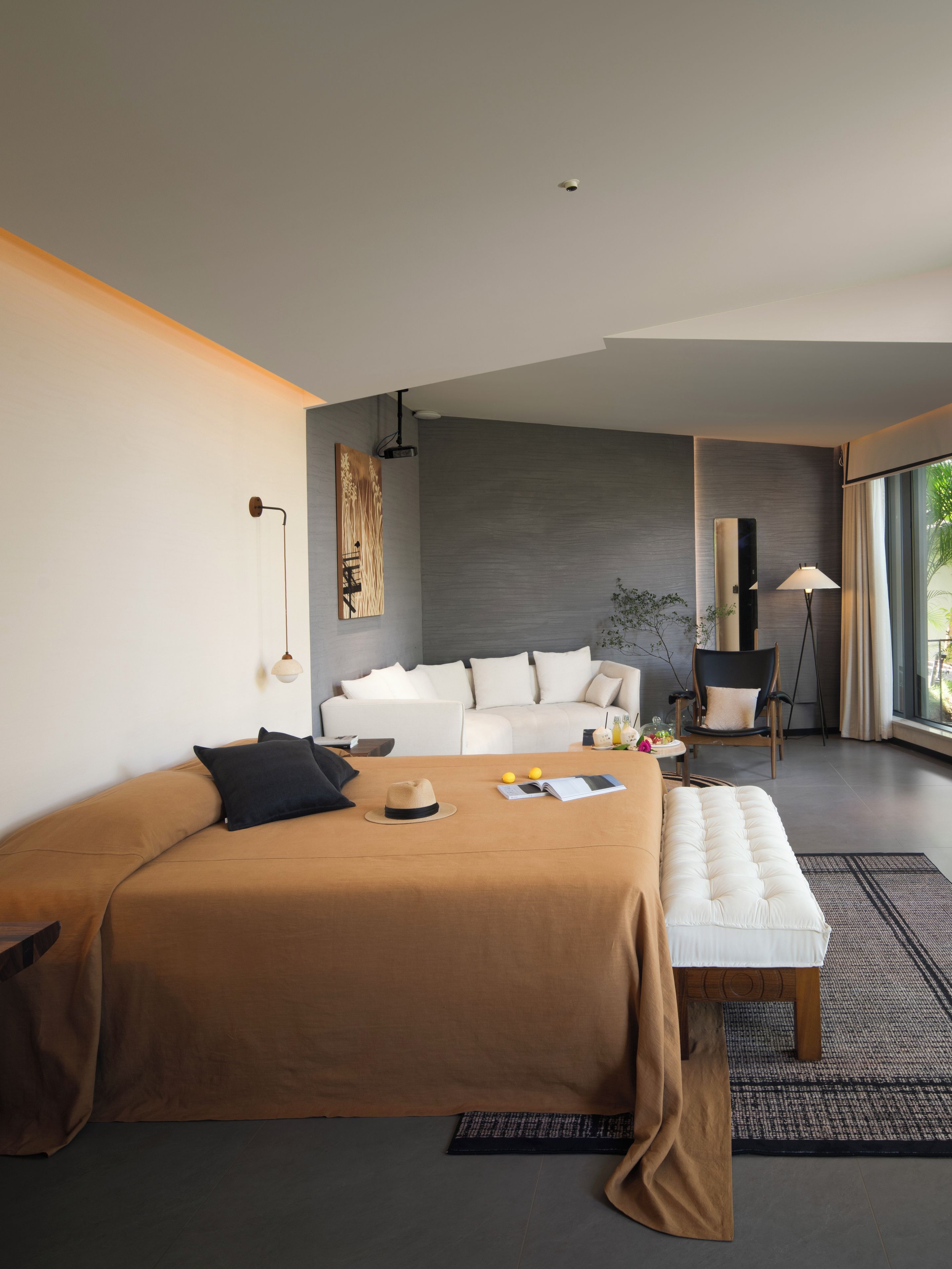 A modern bedroom with a large bed, a sofa, a bench, and a chair. There is a window providing a view of the outdoors.