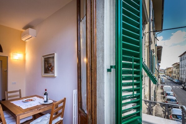 Ein Balkon mit Blick auf eine Straße, ein Esstisch mit einer Weinflasche und ein gerahmtes Bild an der Wand.