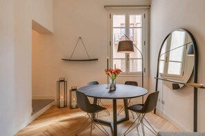 Un comedor moderno con una mesa redonda, sillas negras, un florero con flores, una lámpara colgante y un espejo grande.