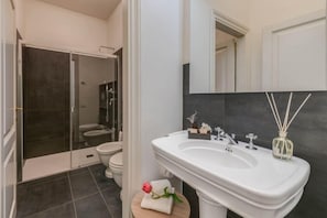 Un baño moderno con un lavamanos blanco, azulejos oscuros, una cabina de ducha de vidrio y un inodoro.