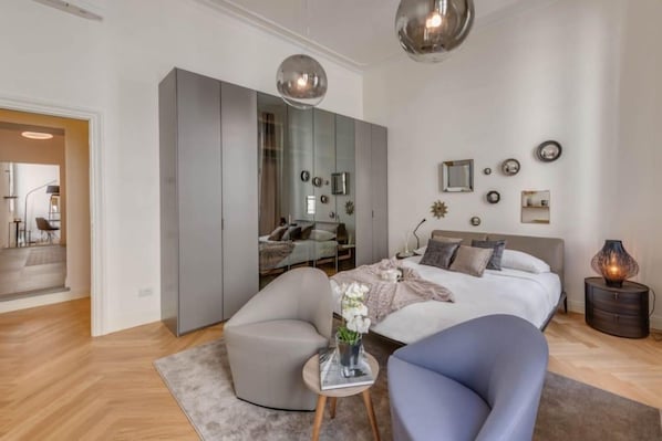 Un dormitorio moderno con una cama, un armario gris, una mesa redonda con un florero y un sillón azul.