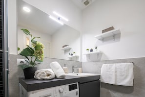 Un baño moderno con un lavamanos blanco, un espejo, una planta en maceta y un perchero para toallas.