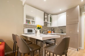 Una cocina moderna con armarios blancos, una isla central con sillas, microondas y refrigerador.