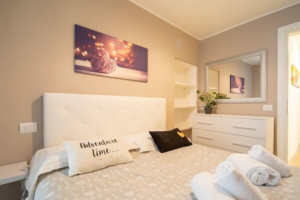 Habitación de hotel con cama, mesita de noche, cómoda, espejo y un cuadro en la pared.