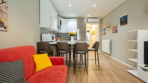 Ein modernes Wohnzimmer mit einem roten Sofa, einem Essbereich mit Stühlen und einer Küche im Hintergrund.