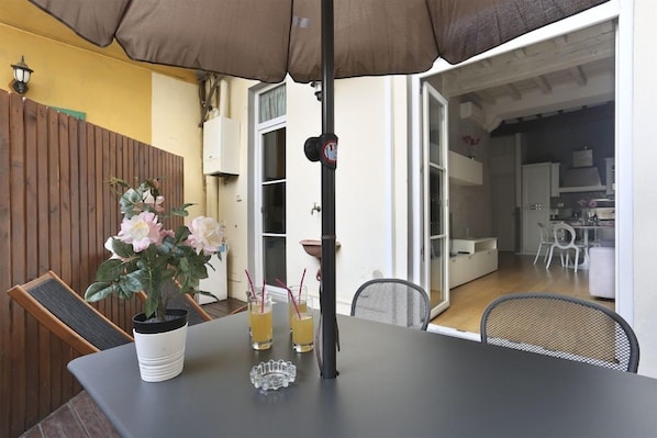 Un área de comedor al aire libre con una mesa, sillas, una planta en maceta y bebidas.