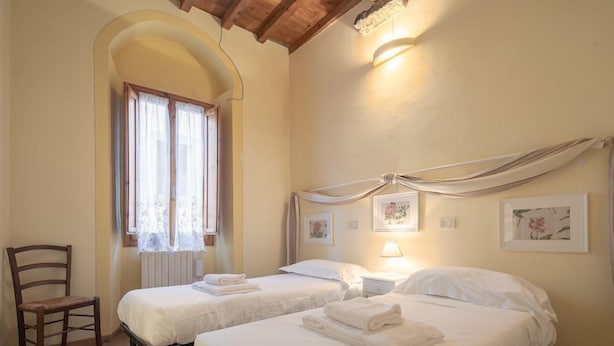 Ein Zimmer mit zwei Betten, einem Sessel und einem Fenster mit Vorhängen.