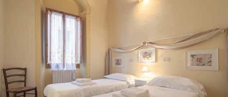 A room with two beds, a chair, and a window with curtains.