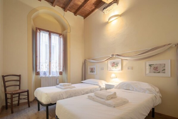 Una habitación con dos camas, una silla y un ventanal con cortinas.