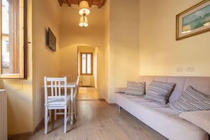 Una sala de estar acogedora con sofá y sillones, una mesa de comedor, un televisor y un pasillo que lleva a otra habitación.