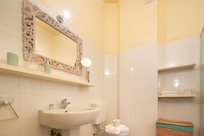 Un baño con lavamanos, espejo, inodoro y estantes.