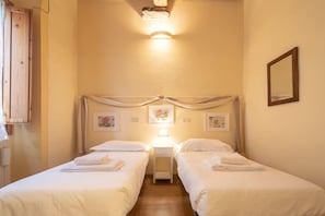 Una habitación de hotel con dos camas, una mesita de noche con lámpara y un espejo en la pared.
