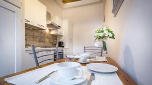 A dining table set with white plates, cups, and cutlery, a vase with white flowers, and a wooden chair. - Arno Apartment B (Florence)
