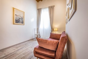 Una habitación con un área de descanso con cojines, un cuadro en la pared, una silla y una lámpara.