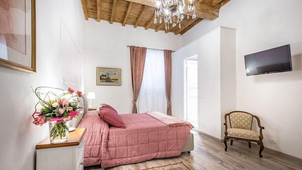 A bedroom with a bed, a chair, a TV, and a chandelier. - Arno Apartment B (Florence)