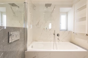 Un baño moderno con ducha envuelta en vidrio, una bañera independiente y pared revestida de mármol.