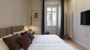 Ein Schlafzimmer mit einem Bett, einem Nachttisch, einem Heizkörper, einem Fenster und einem an der Wand montierten Fernseher.