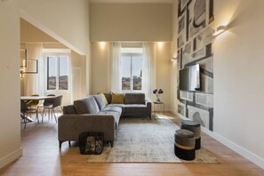 Una sala de estar moderna con un sofá seccional, un comedor con sillas y un ventanal con vistas a la ciudad.