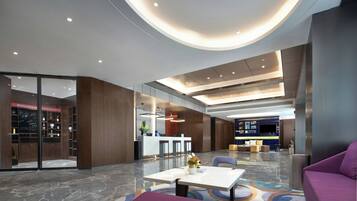 A modern hotel lobby with a reception desk, seating area, and a large screen.