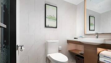 A modern bathroom with a toilet, sink, and mirror. There are framed pictures on the wall and a basket under the sink.