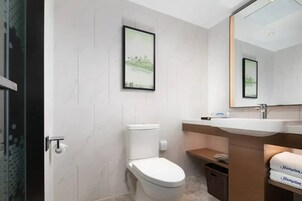 A modern bathroom with a toilet, sink, and mirror. There are framed pictures on the wall and a basket under the sink.