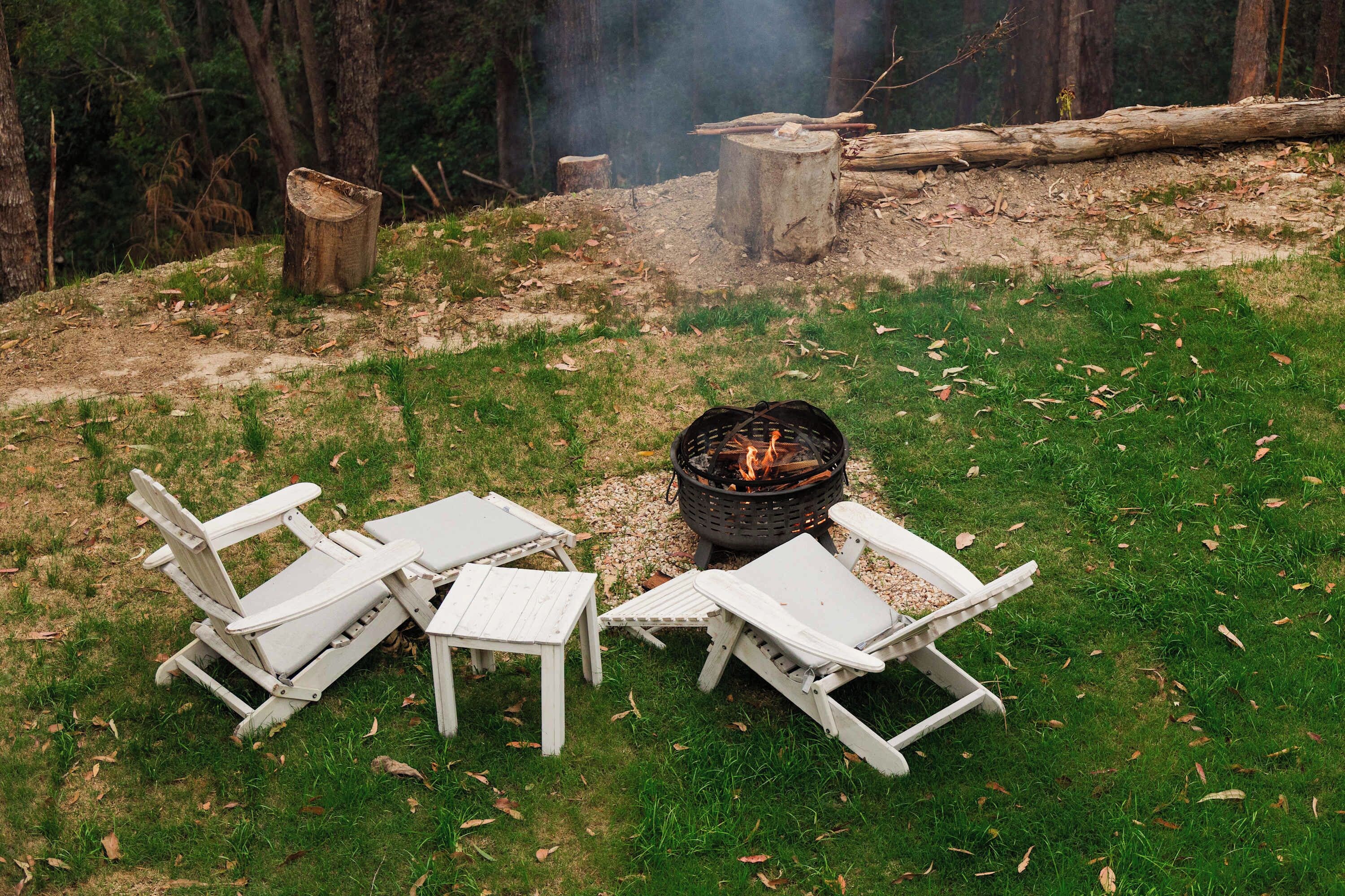 Ein Campingplatz mit Feuerstelle, umgeben von weißen Stühlen und Tischen.