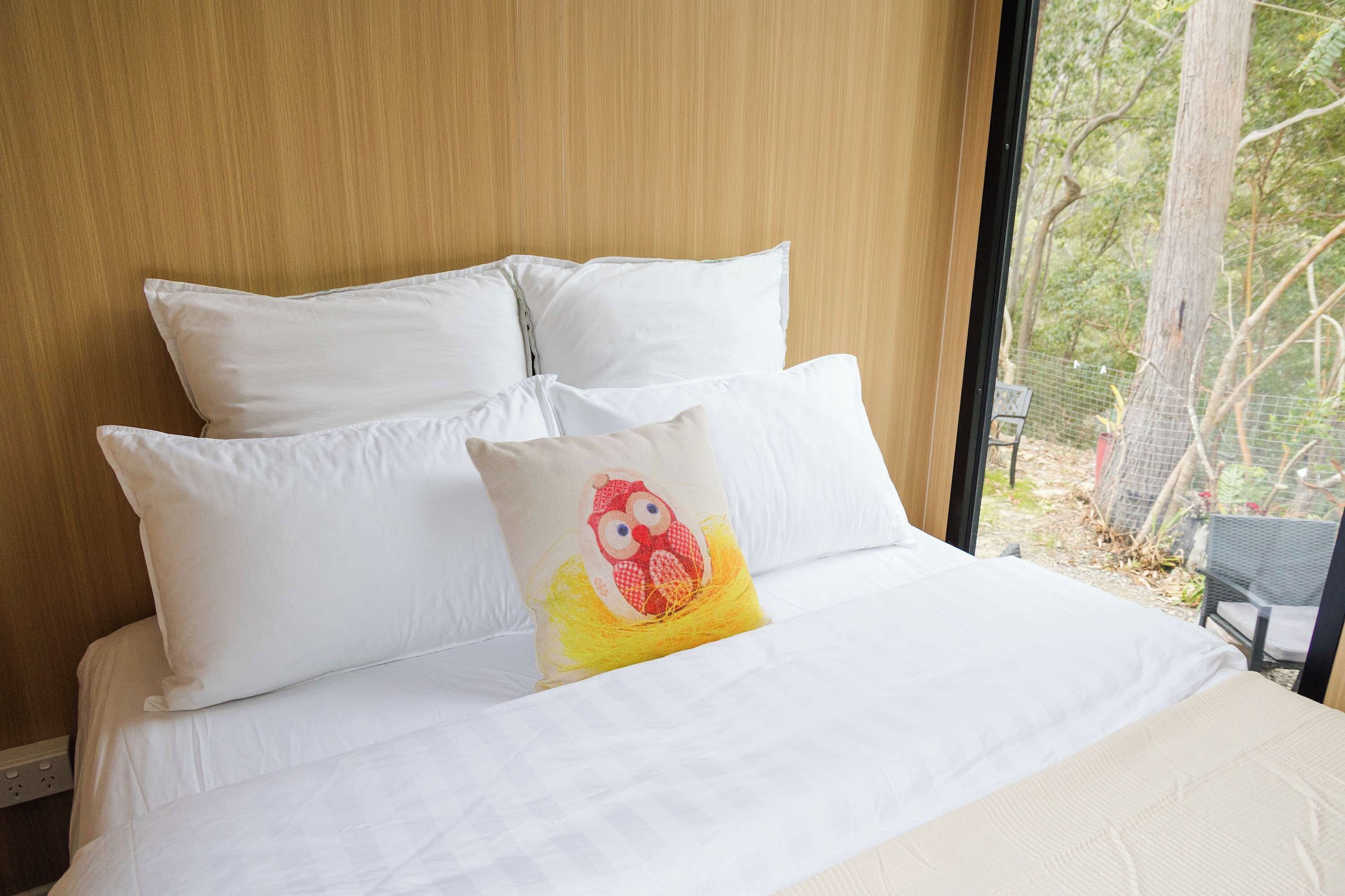 Ein Bett mit weißer Bettwäsche und Kissen, wobei ein Kissen ein rotes und gelbes Eulenmotiv zeigt.
