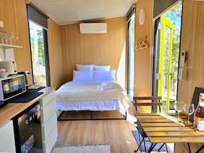 A compact room with a bed, a small table, a microwave, and a window. - GC Hinterland Hideaway by Tiny Away (Bonogin)