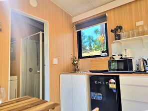 A compact kitchen with a built-in microwave, toaster, and refrigerator. A window with a view of palm trees is above the sink.