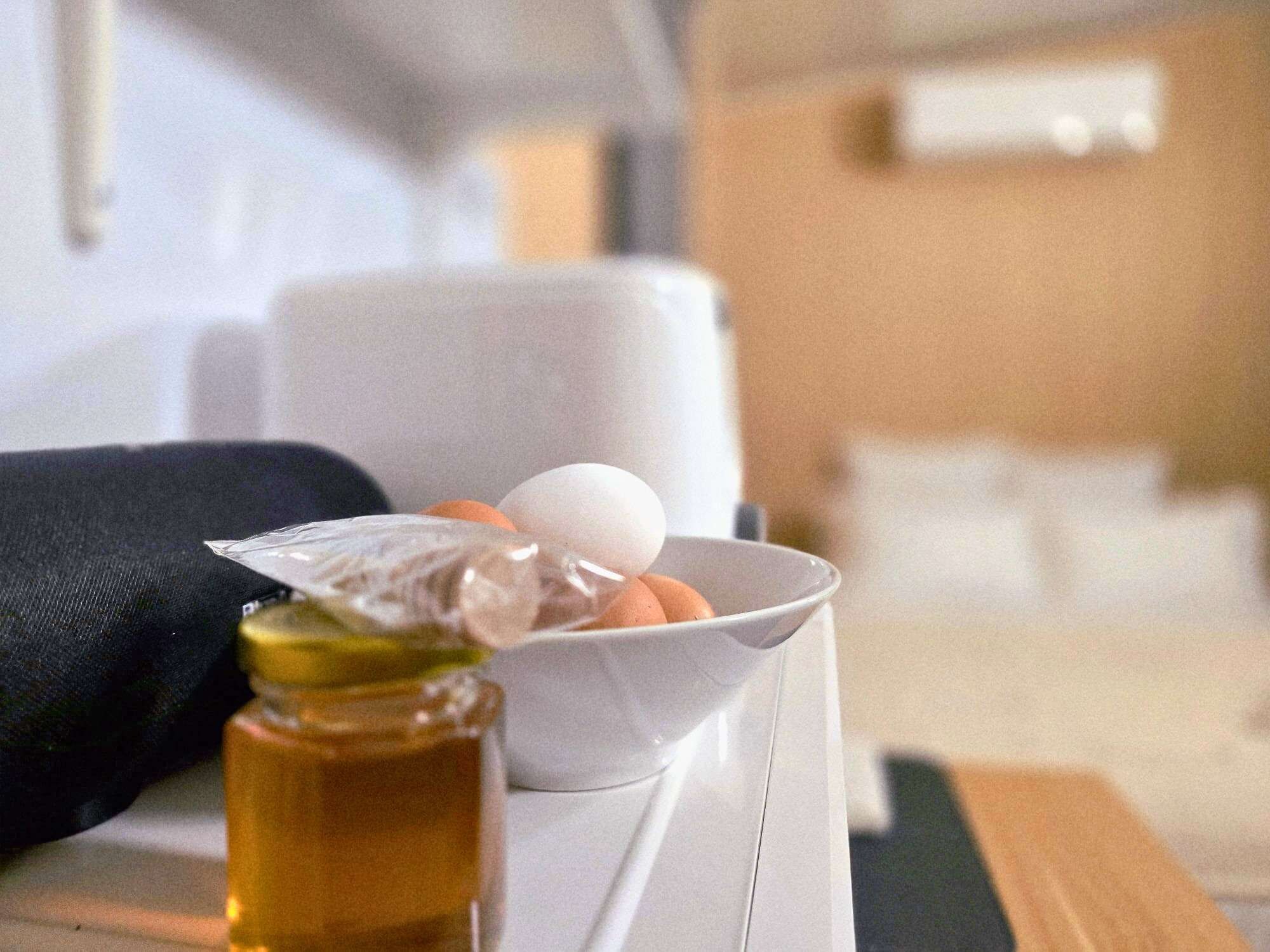 Eine weiße Schüssel mit Eiern und einer Flasche Öl auf einem Tisch.