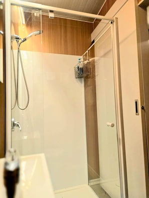 A glass-enclosed shower with a metal rack, a white sink, and a wooden panel wall. - GC Hinterland Hideaway by Tiny Away (Bonogin)