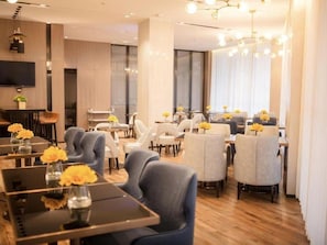 A modern hotel dining area with multiple tables and chairs, a flat-screen TV mounted on the wall, and a chandelier. - Echarm Hotel Xiantao Stadium (Beijing)