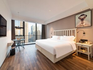 A hotel room with a large bed, a desk, a chair, a view of the city, and a mounted artwork. - Borrman Hotel (Jinan)