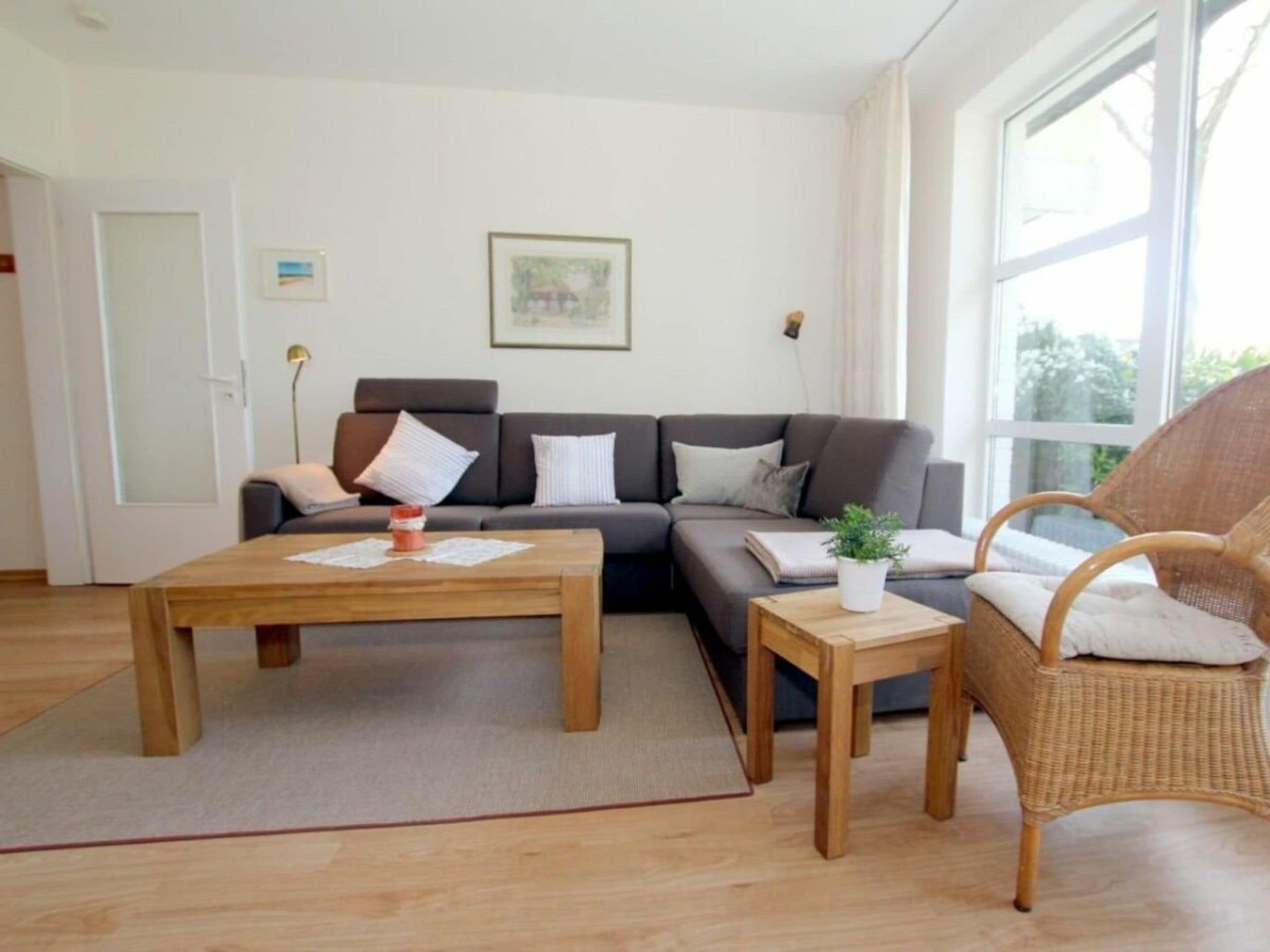 A modern living room with a sofa, two coffee tables, a wicker chair, and a large window.