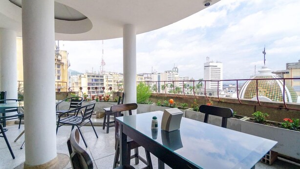 An outdoor seating area with tables and chairs, overlooking a cityscape with buildings and a dome structure. - Ayenda Astoria Real (Cali)
