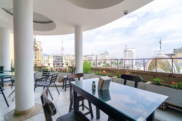 An outdoor seating area with tables and chairs, overlooking a cityscape with buildings and a dome structure. - Ayenda Astoria Real (Cali)