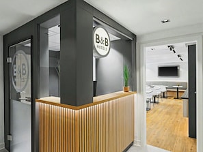 Un comptoir d’accueil orné d’un panneau B&B Hotels, avec un décor en lambris de bois et une plante en pot.