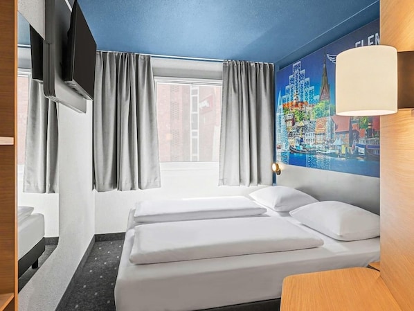 A hotel room with a bed, curtains, a window, a wall-mounted TV, and a lamp. - Ibis Budget Flensburg City (Flensburg)