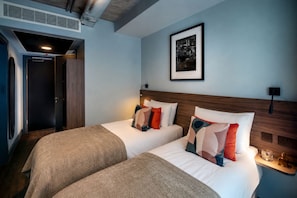 Une chambre d’hôtel avec deux lits, un tableau encadré au mur et une porte donnant sur une autre pièce.