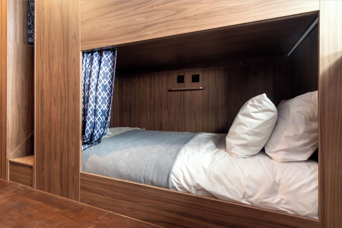 Un lit superposé avec une structure en bois, un rideau à motifs et un mur orné d’un motif géométrique.