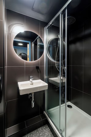 Une salle de bain moderne avec une douche à parois de verre, un lavabo blanc et un miroir doté d’un cadre circulaire.
