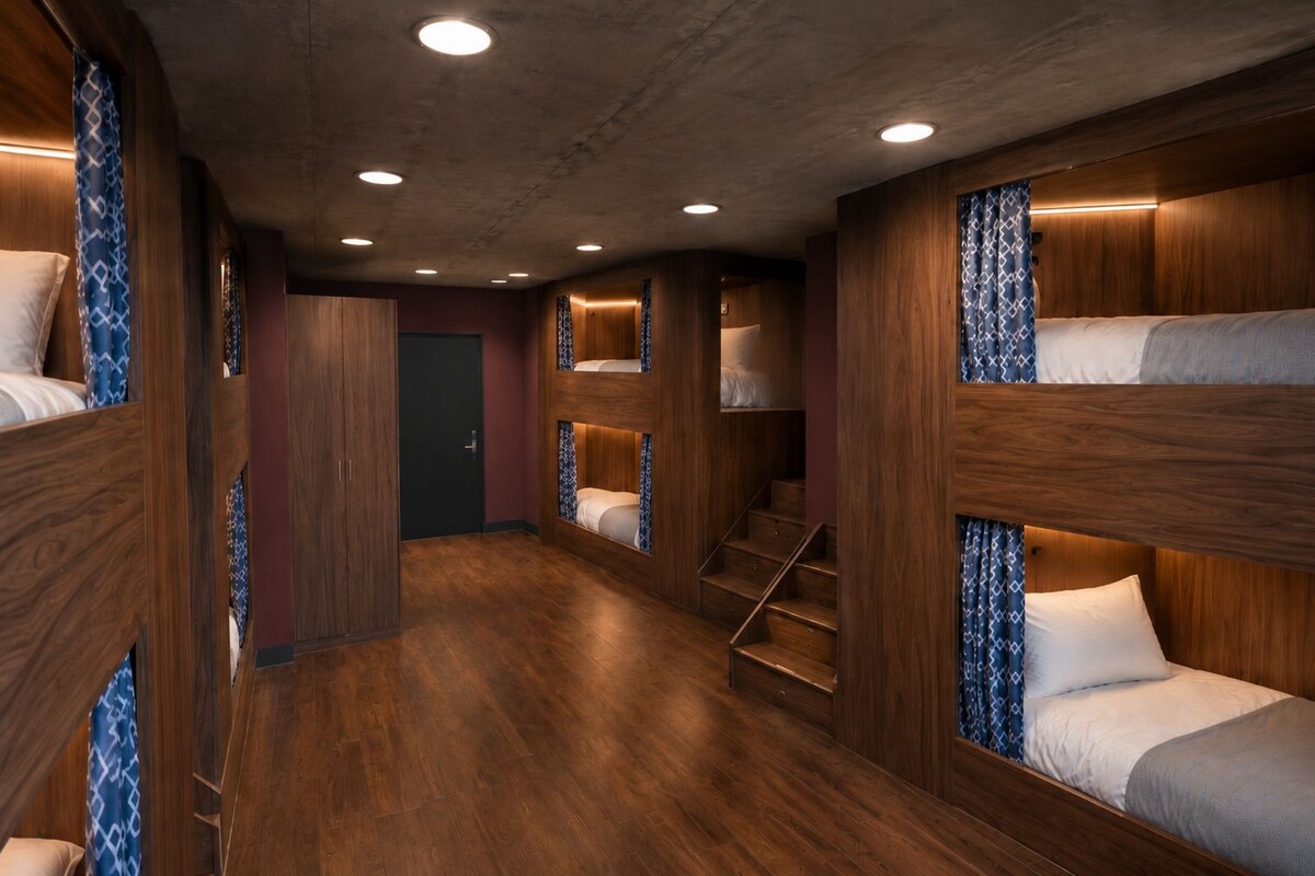 Une chambre d’hôtel avec des lits superposés, un plancher en bois et un escalier.