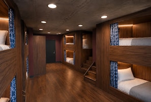 Une chambre d’hôtel avec des lits superposés, un plancher en bois et un escalier.