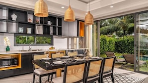 Una cocina moderna con comedor, ventanas amplias y vistas a una piscina y follaje.